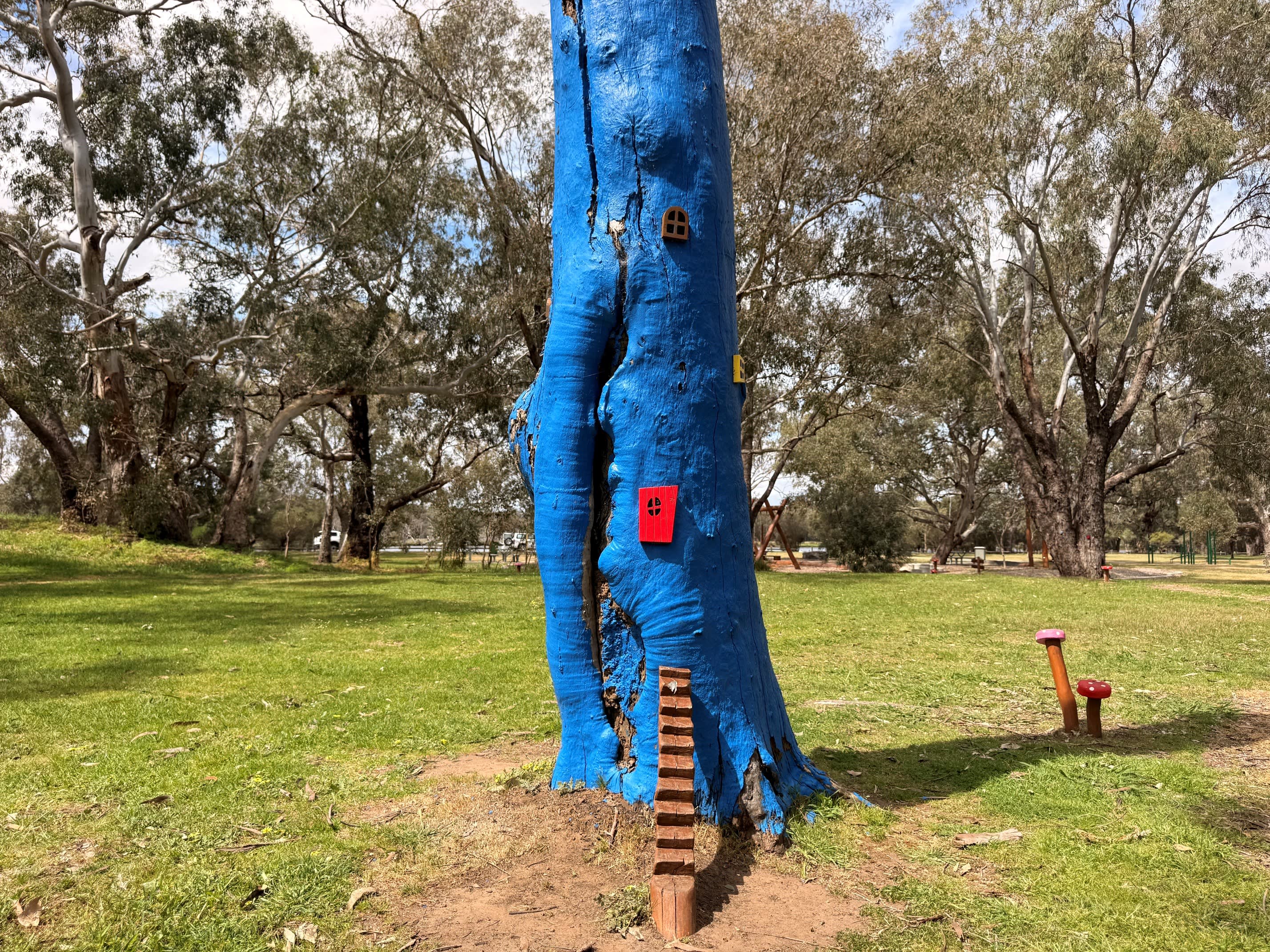 Blue tree with fairy steps leading up to it and painted toadstool figurines in grass.