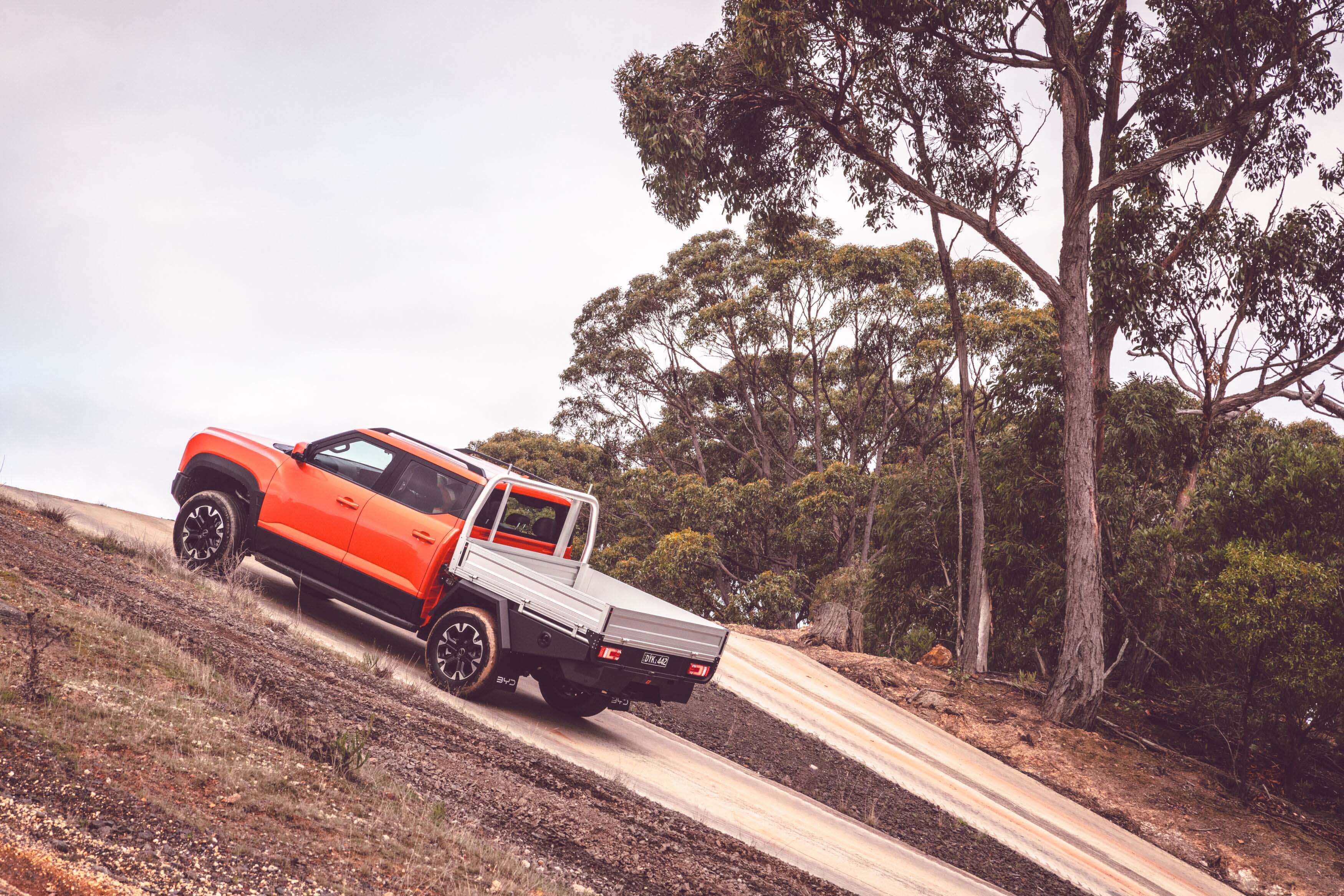 An orange BYD ute driving up a steep incline with trees in the background.