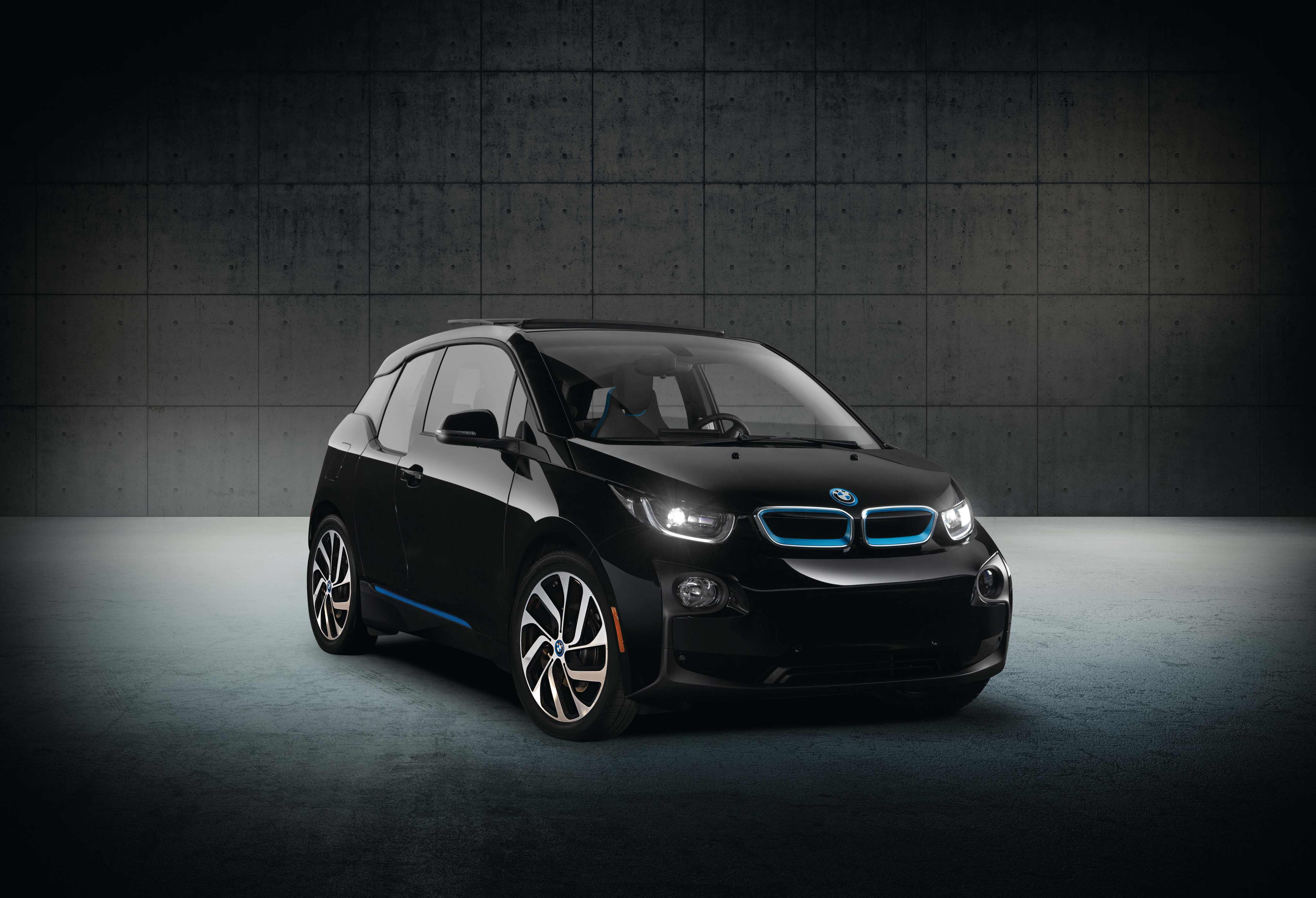 A black 2016 BMW i3 under a spotlight in a studio with a concrete floor and wall behind.