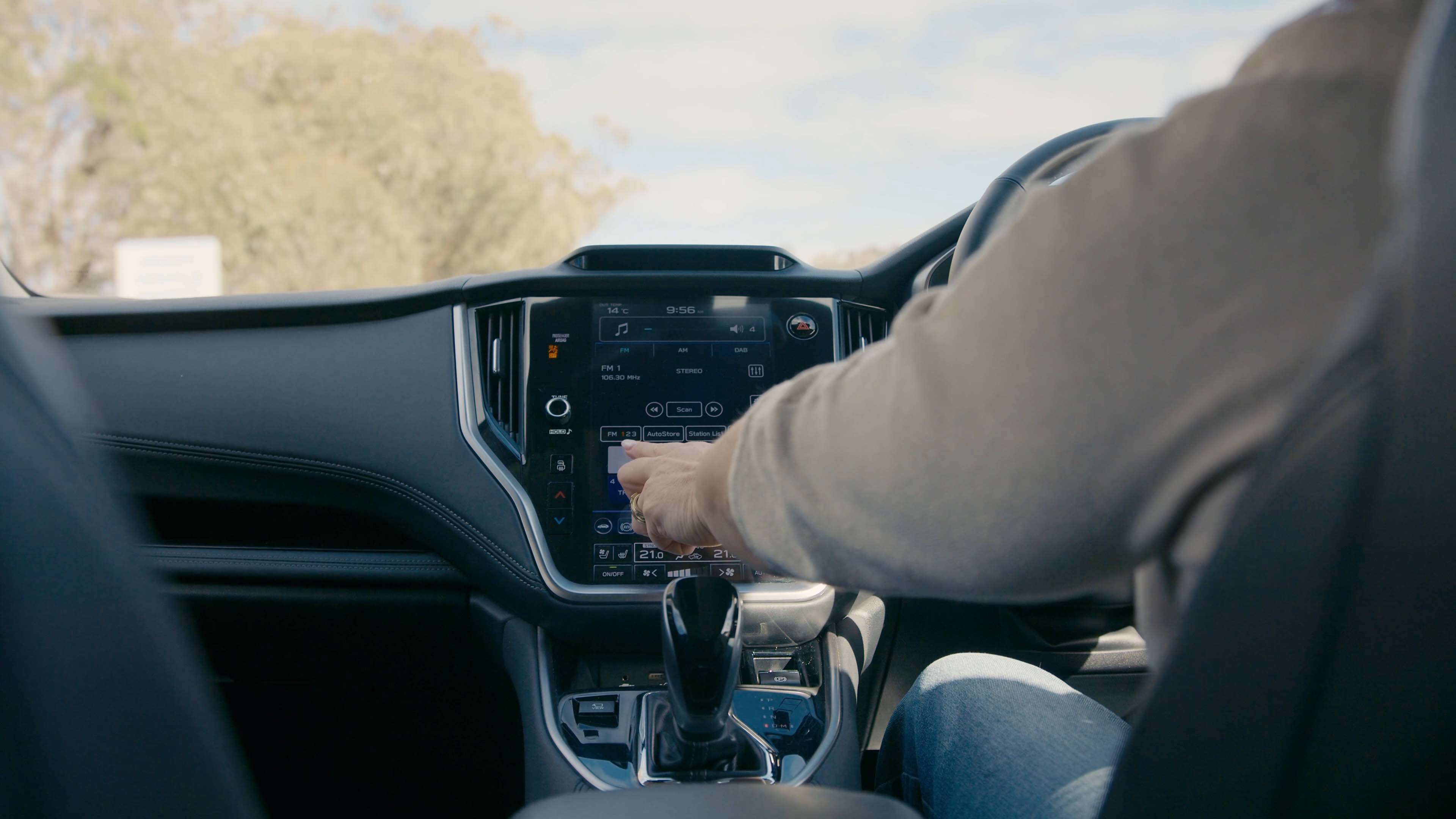A driver reaches their hand towards the dashboard of the car.