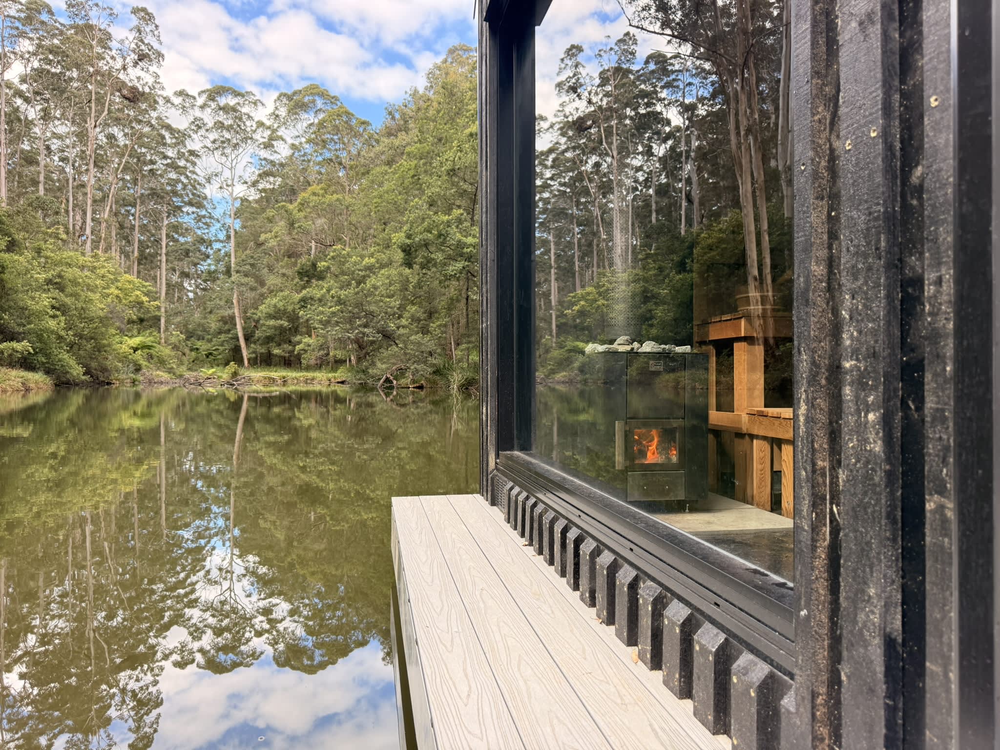 Timber deck over water with sauna fireplace view through large glass window.