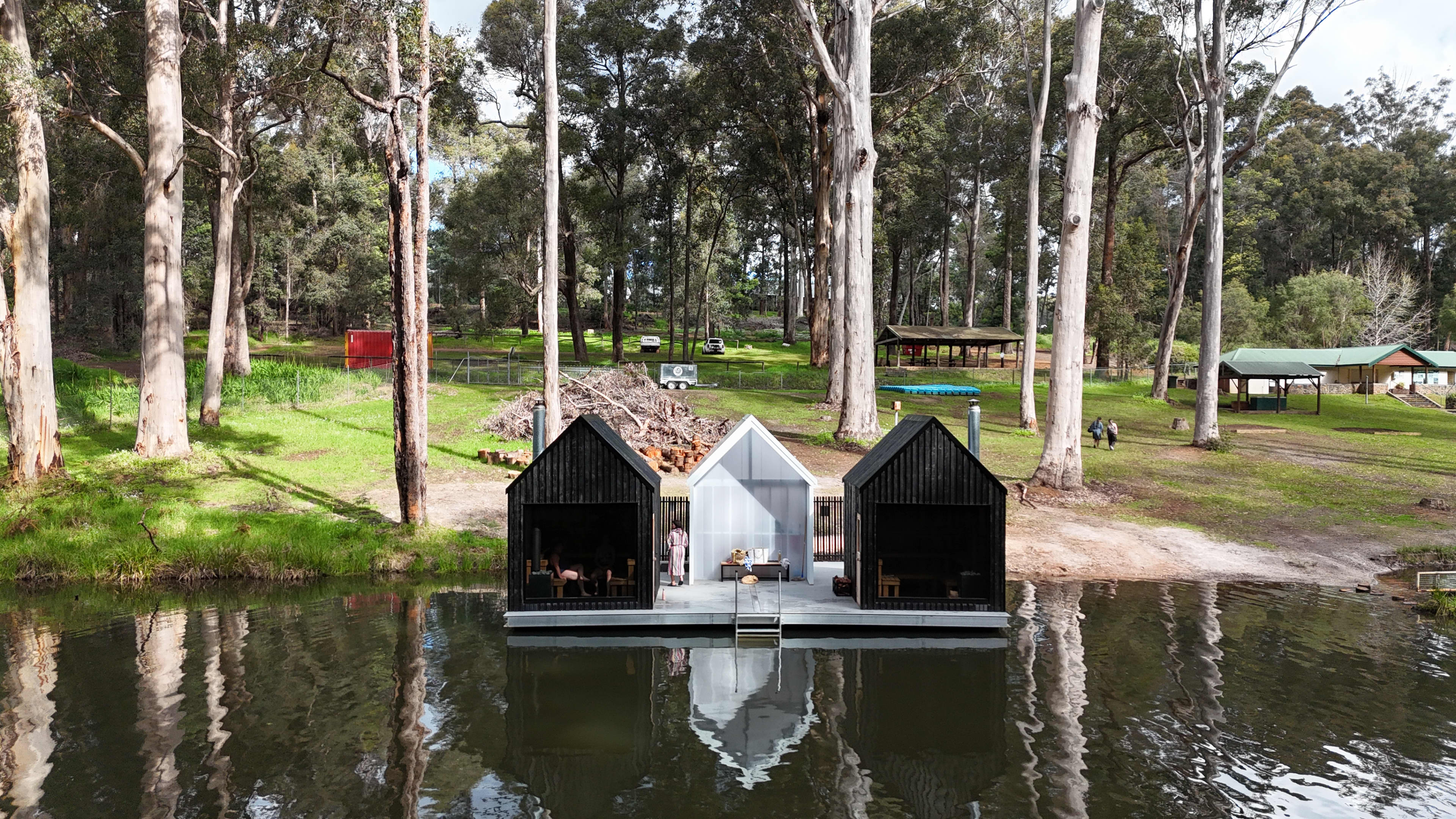 A natural swimming hole surrounded by trees with a small sauna floating by river bank.