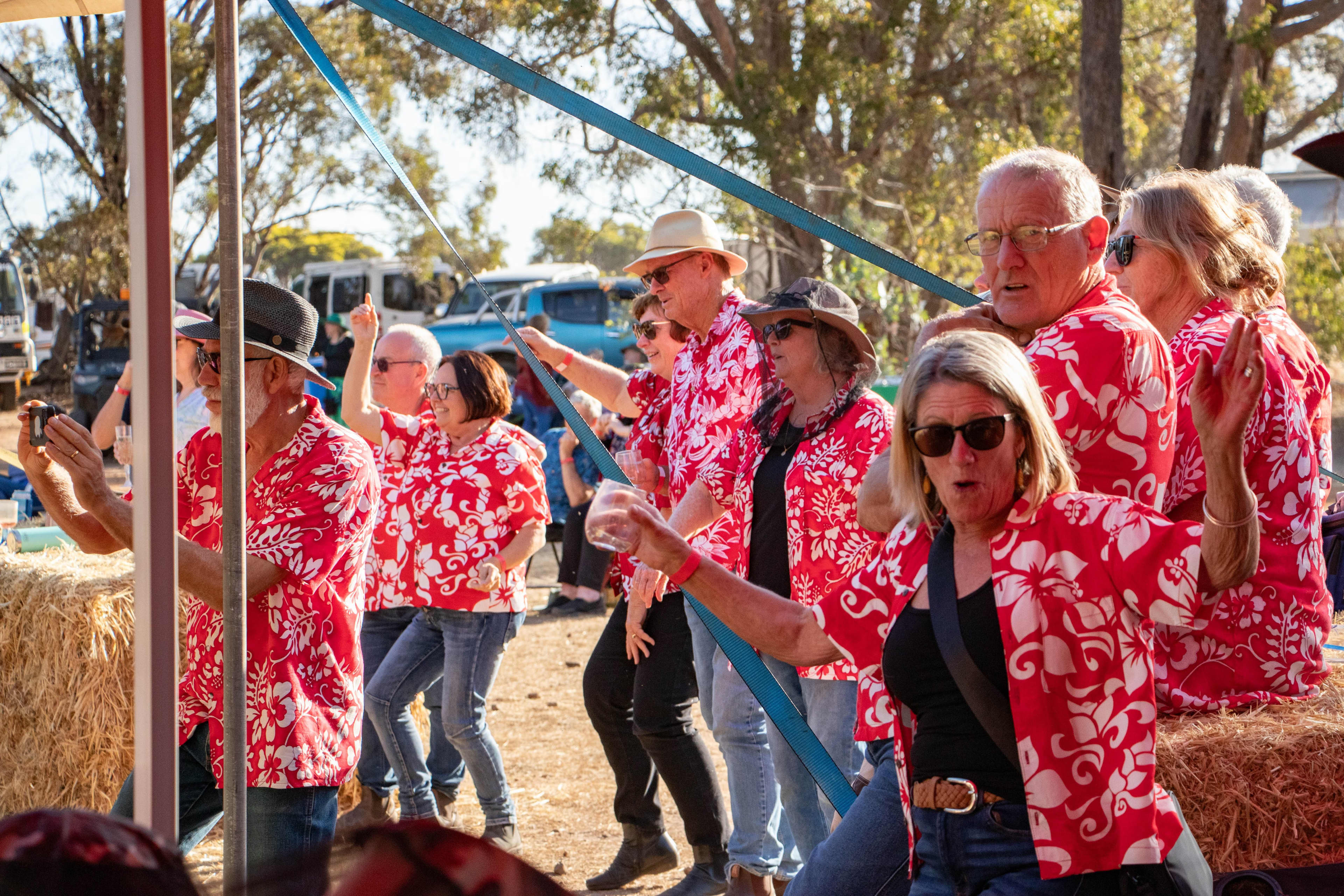 An image of a line-up of festival goers wearing red patterned shirts dancing with hay bales in the background.