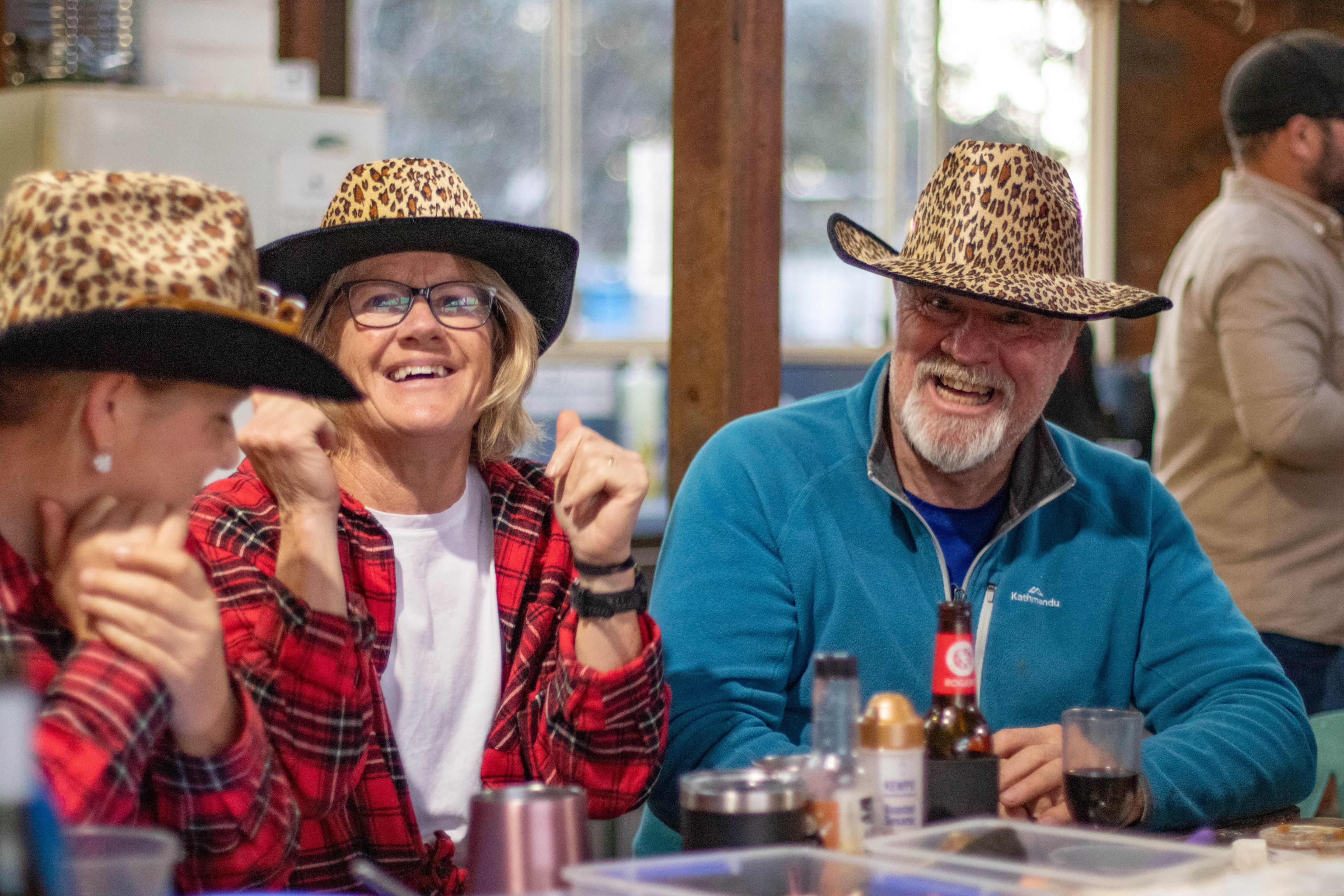 A couple with a man wearing a bright blue jumper and a female wearing a bright red checkered shirt, both wearing matching leopard print cowboy hats smiling.