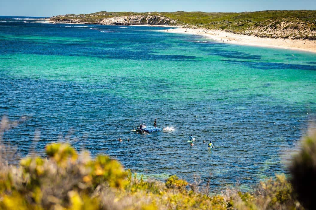 A small blue pontoon in a protected bay, with people jumping off and swimming around it.