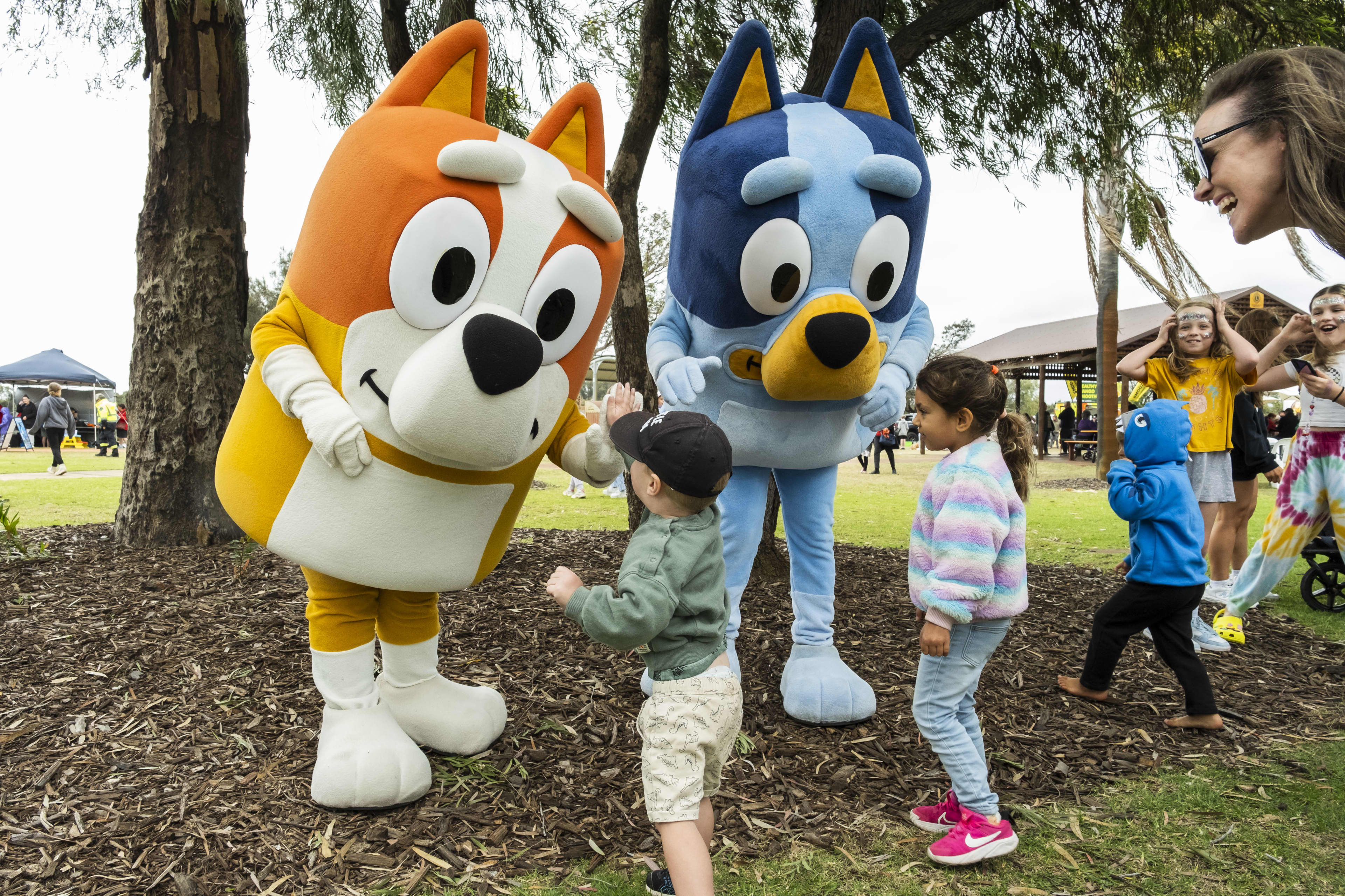 A community event where children are interacting with mascot characters Bluey and Bingo from the children's television show.