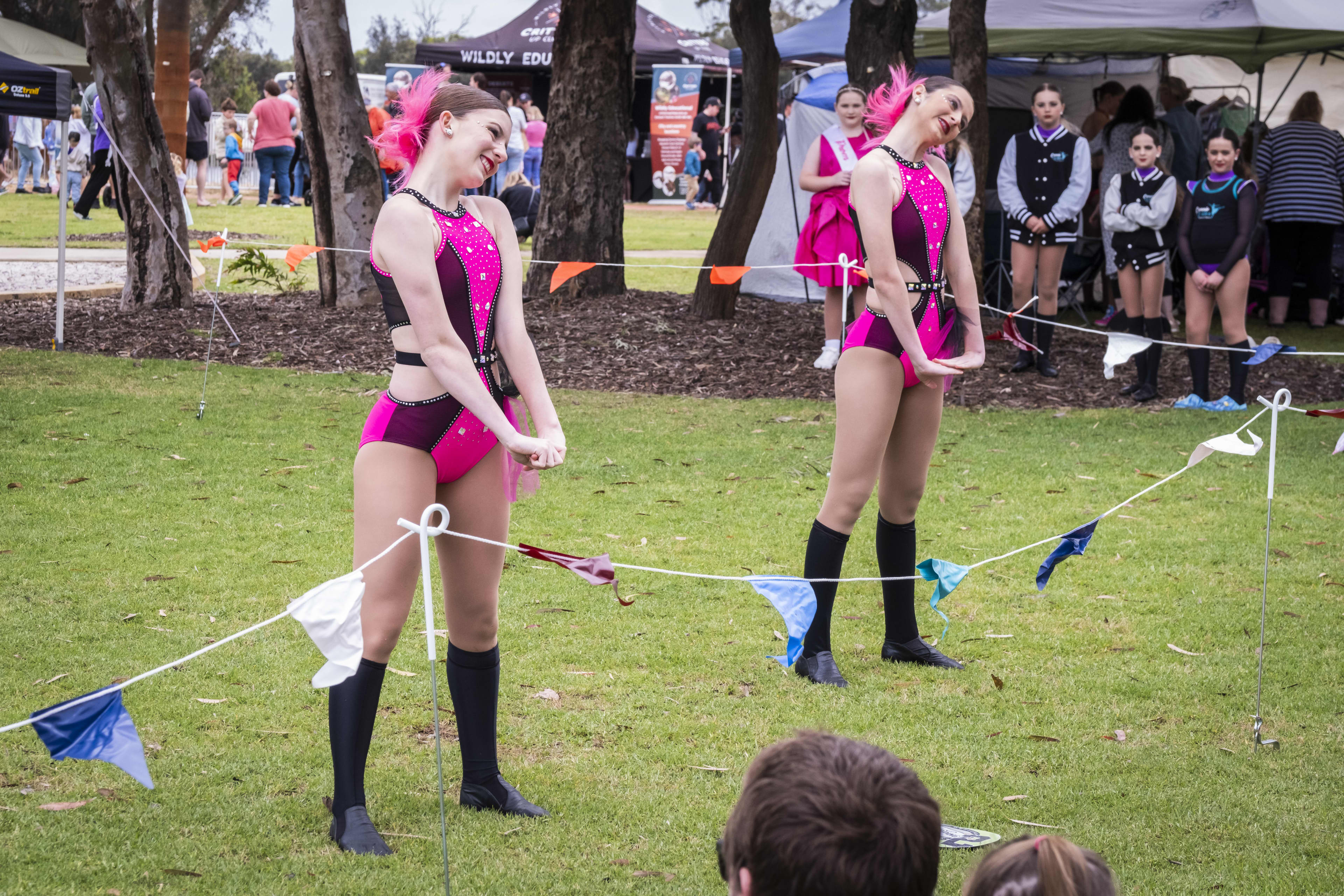 Two young females in bright pink dance outfits, performing on lush green lawn.