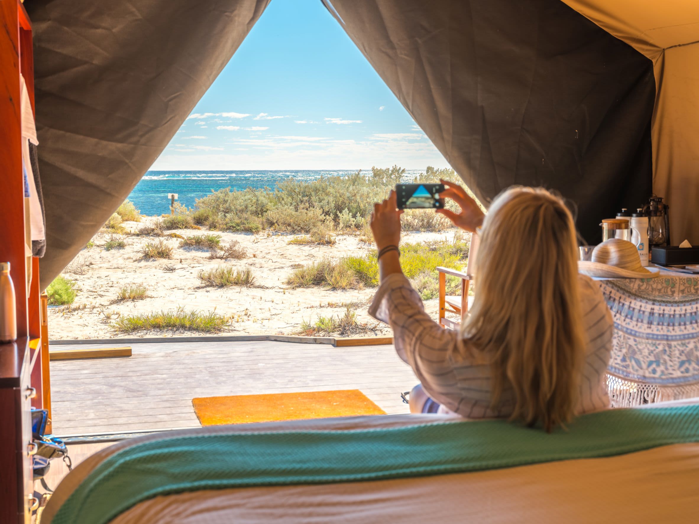 A first-person view from inside a tent or camper, where a person is using a smart phone to take a photo of the landscape outside.