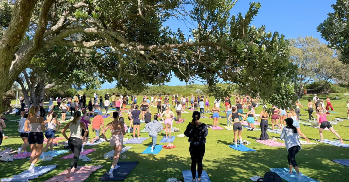 Group of people outdoors in sunshine doing yoga on colourful yoga mats.