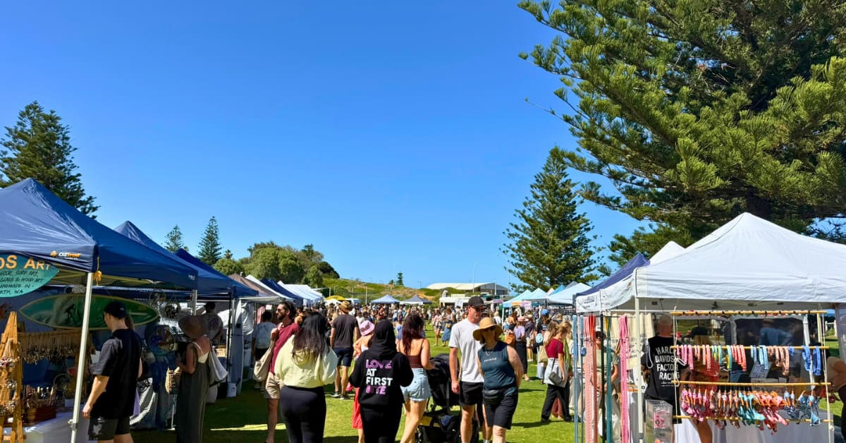 People browsing market stalls on sunny day outside.