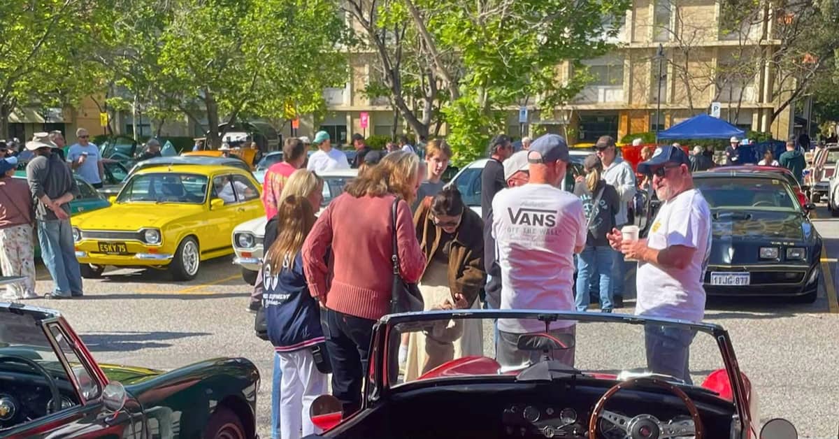 Group of people gathered together around cars.