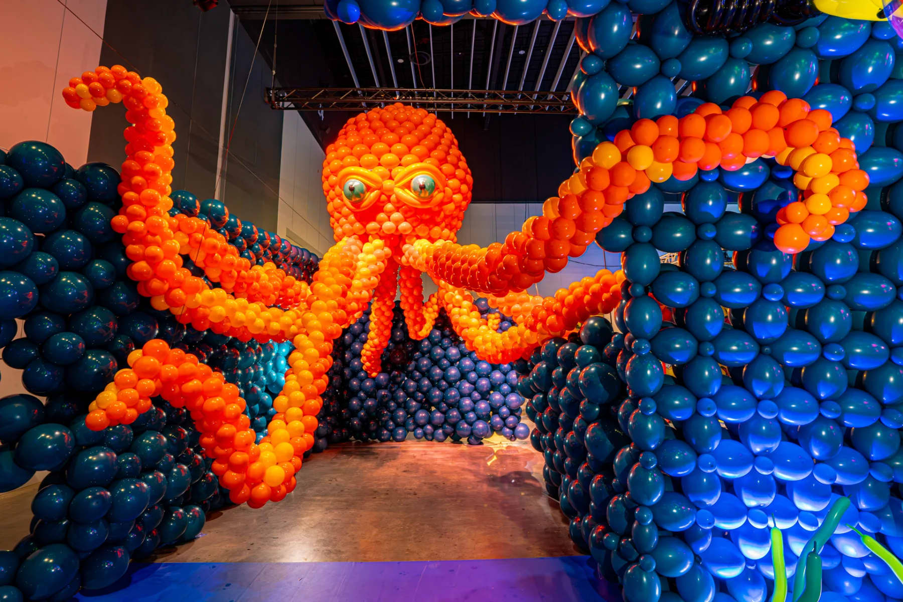 Orange balloons in the shape of a giant octopus under the ocean made from blue balloons.