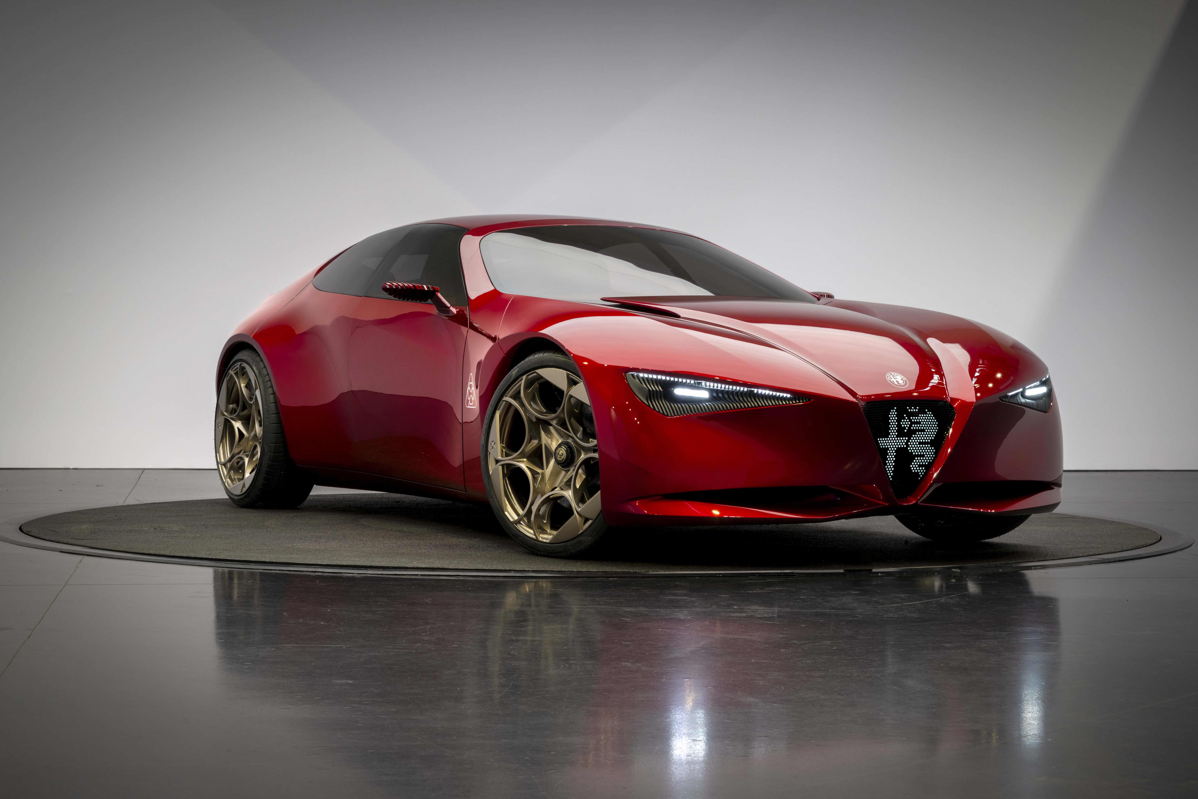 A shiny red sports car on a circular turntable under studio lighting.