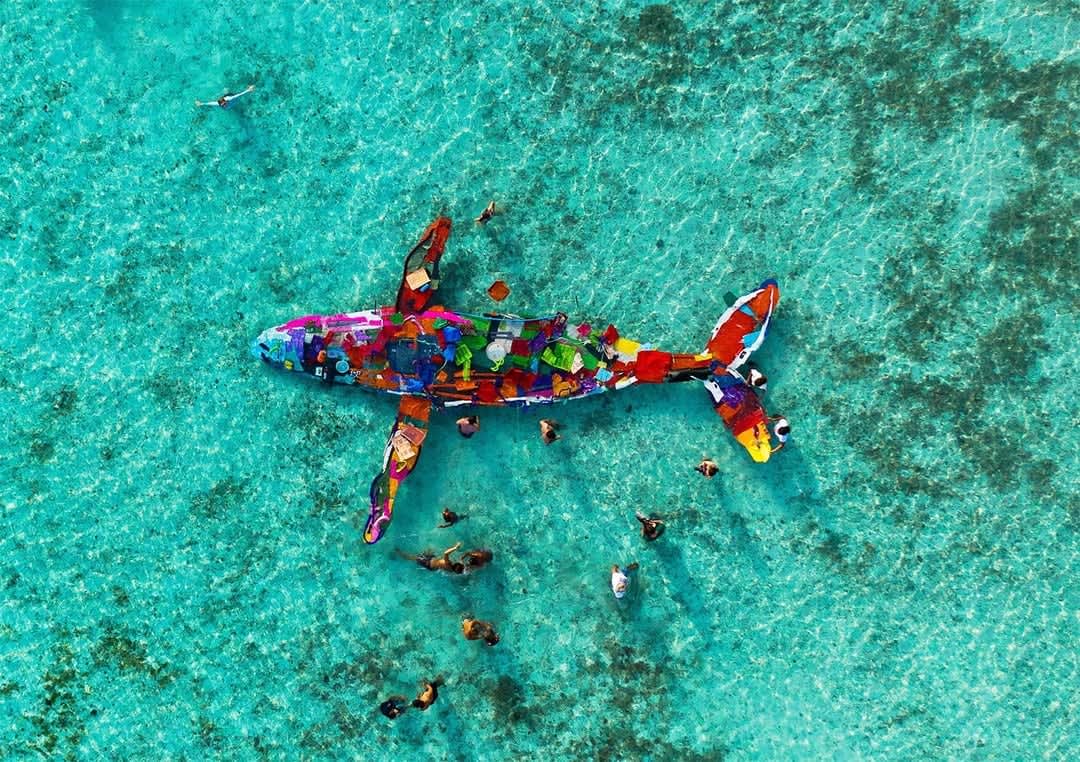 Large colourful plastic whale sculpture in ocean.