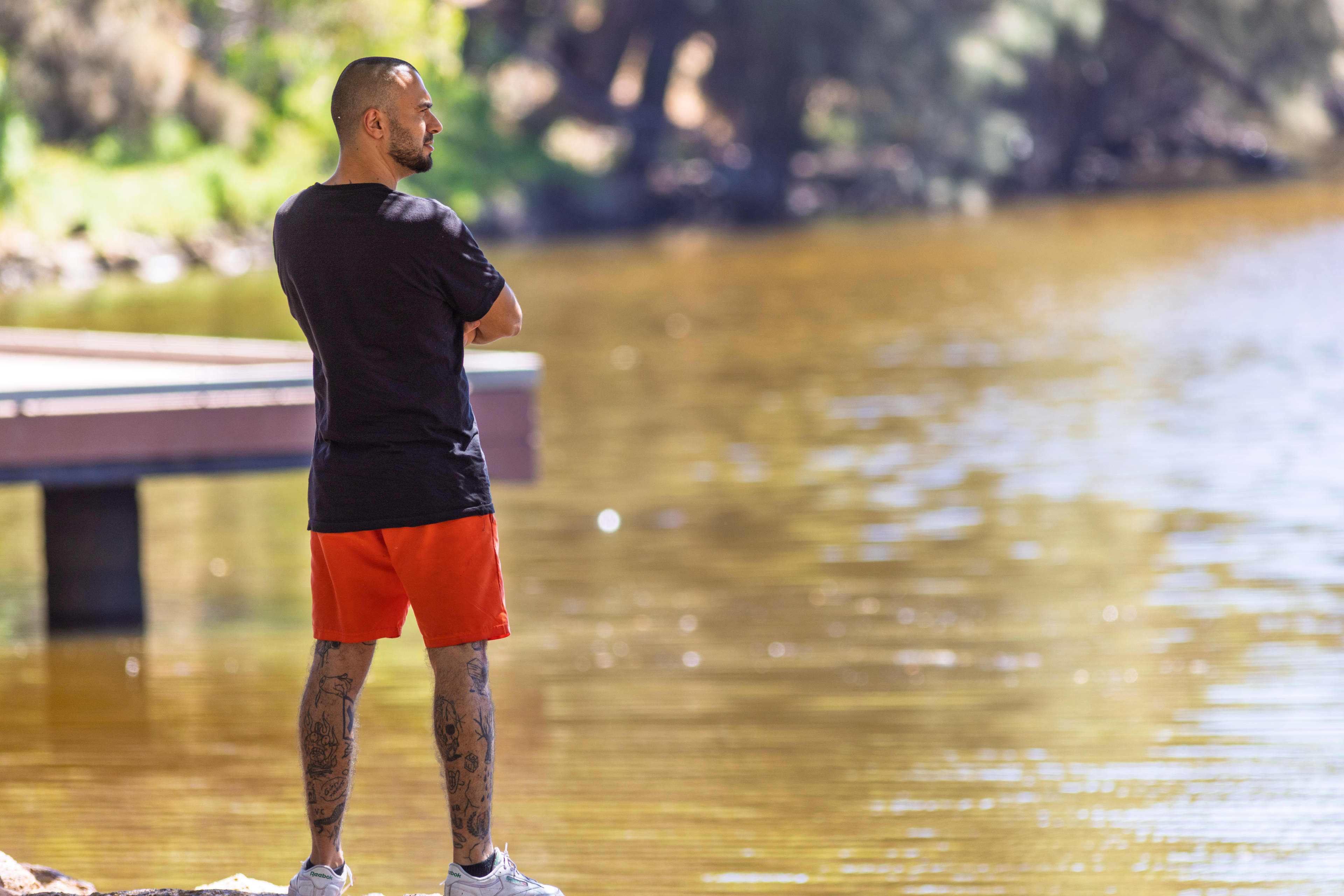 Man standing in red shorts and black tshirt looking over water.