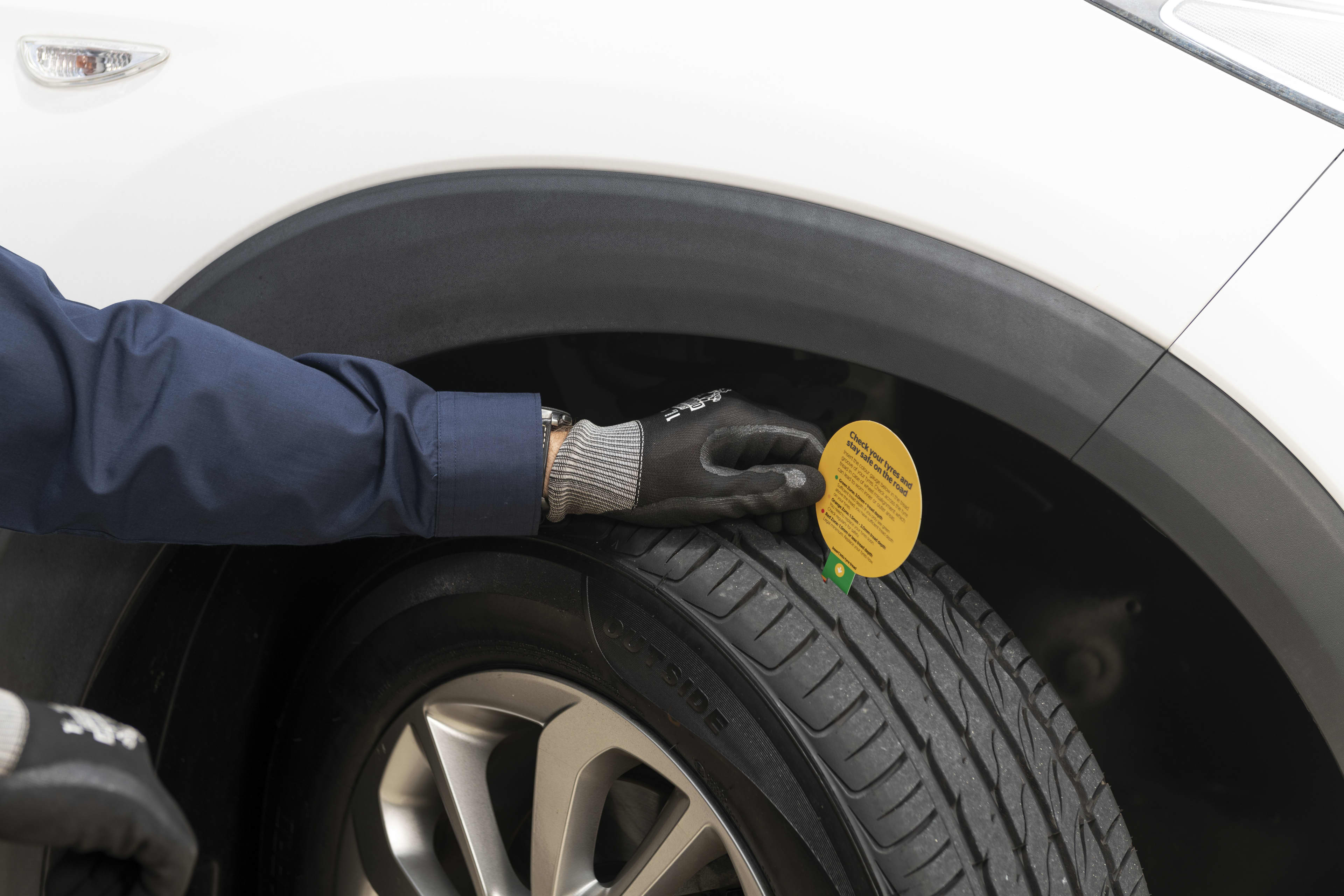A person with a long-sleeved navy shirt and a black and grey glove holds a yellow tag on a car tyre.