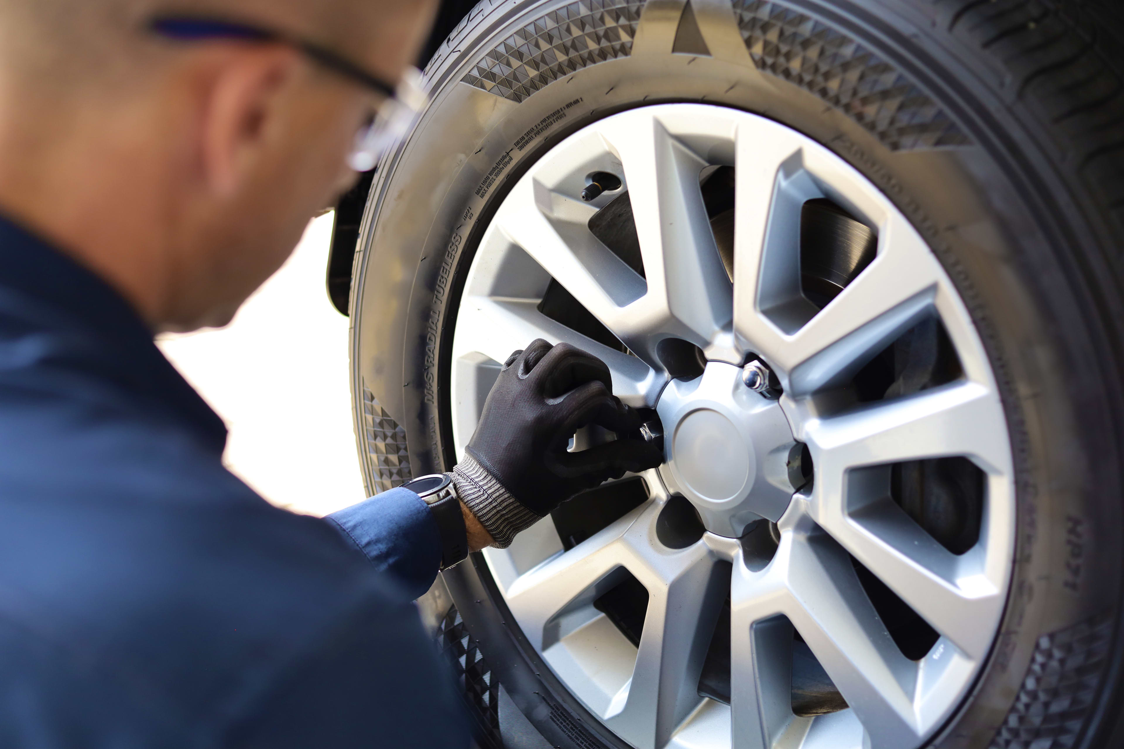 A man wearing navy blue shirt, safety glasses and black and grey gloves makes adjustments to a car tyre.