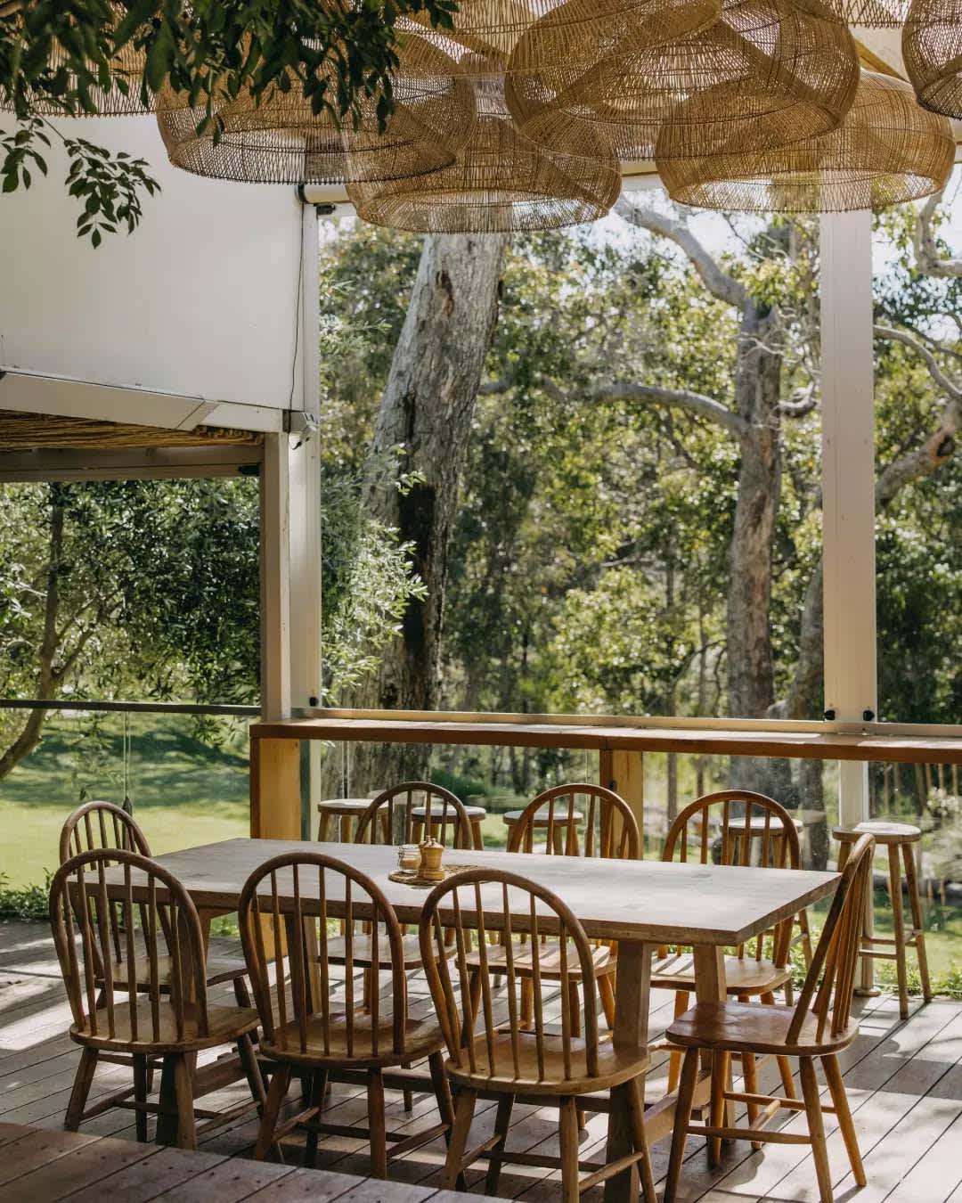 A restaurant table with wooden chairs on a balcony, overlooking grass and trees.