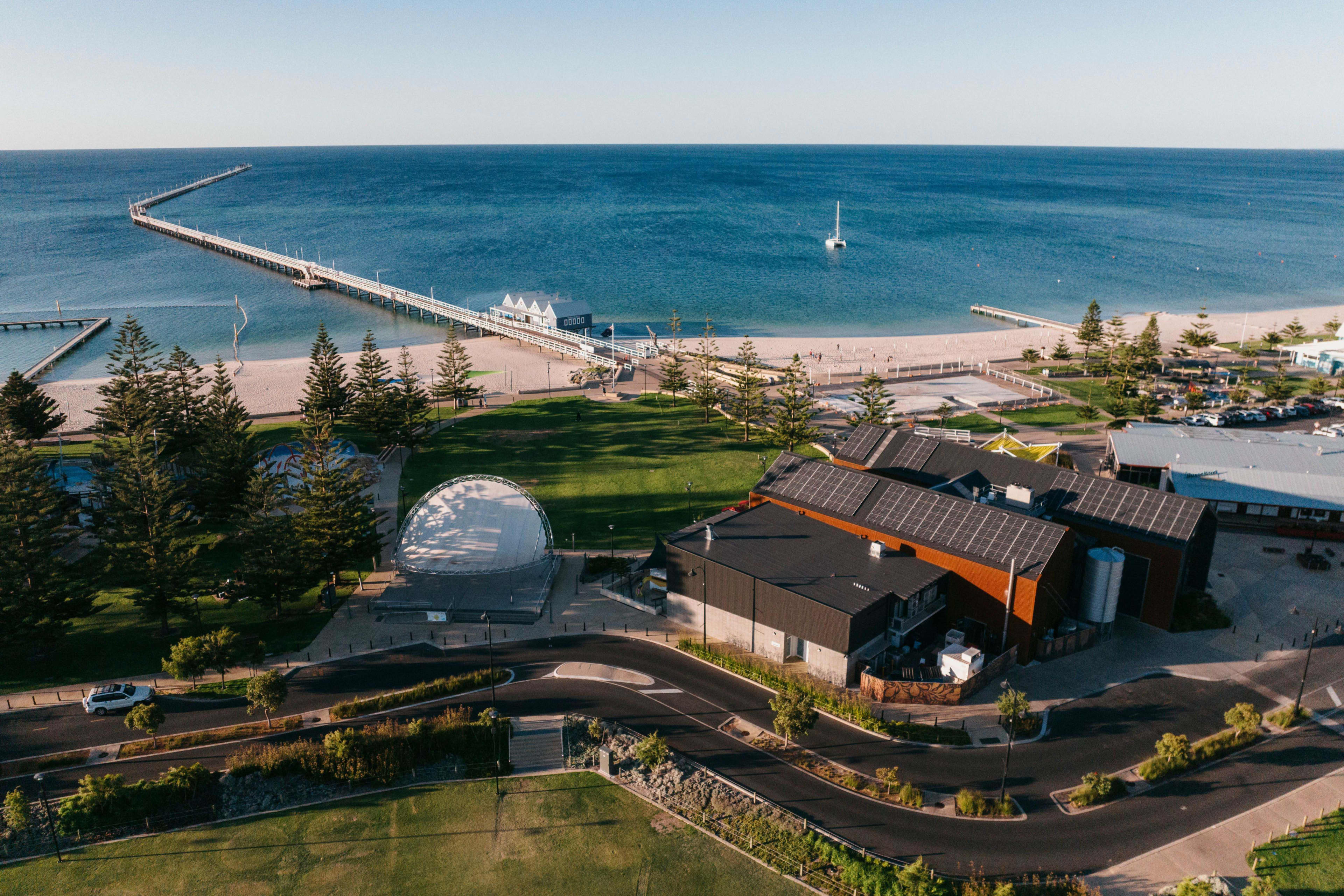 An aerial shot of buildings with blue ocean and a long jetty in the background.