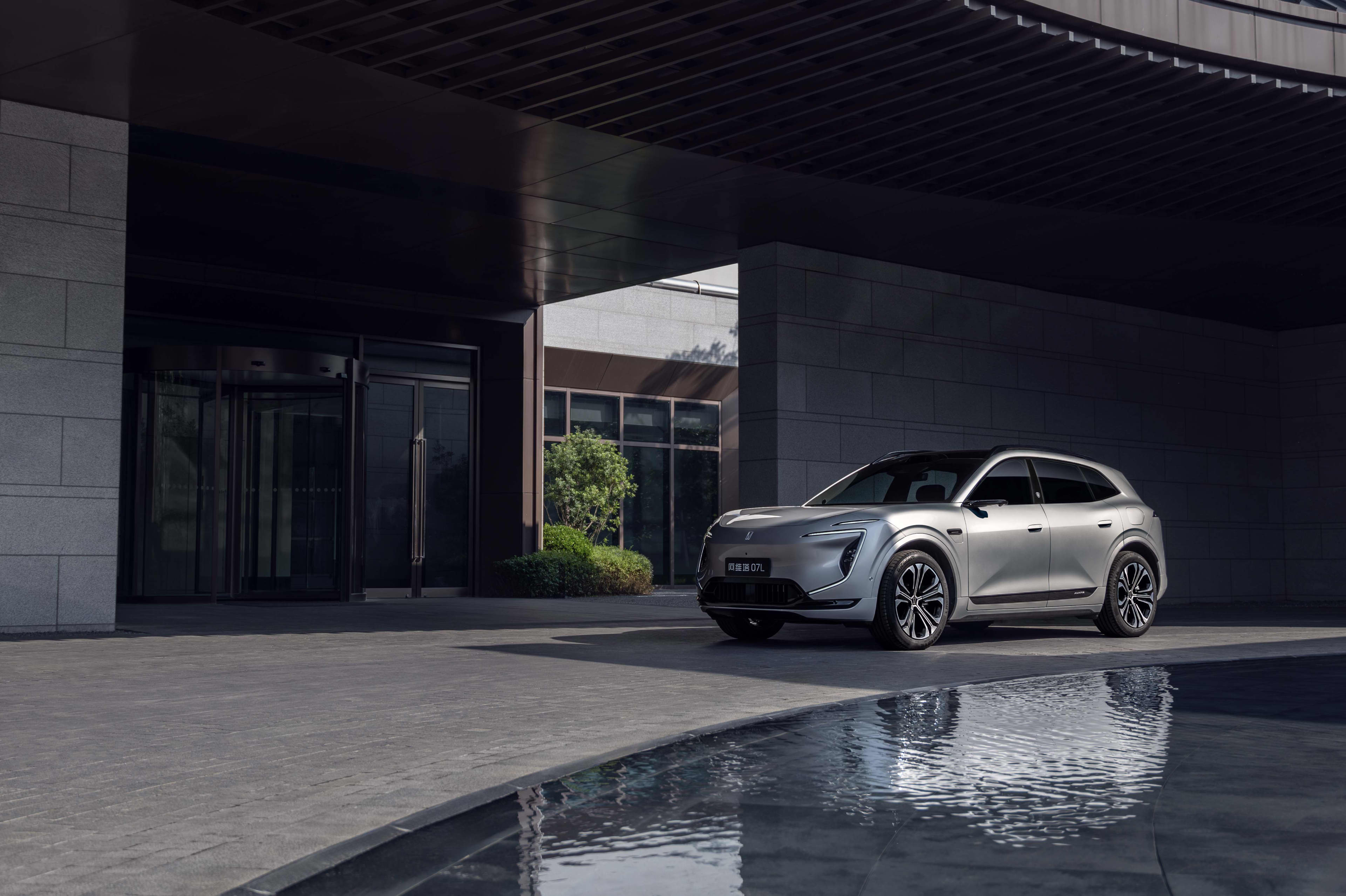 A silver SUV parked in front of a dark coloured building with a water feature beside it.