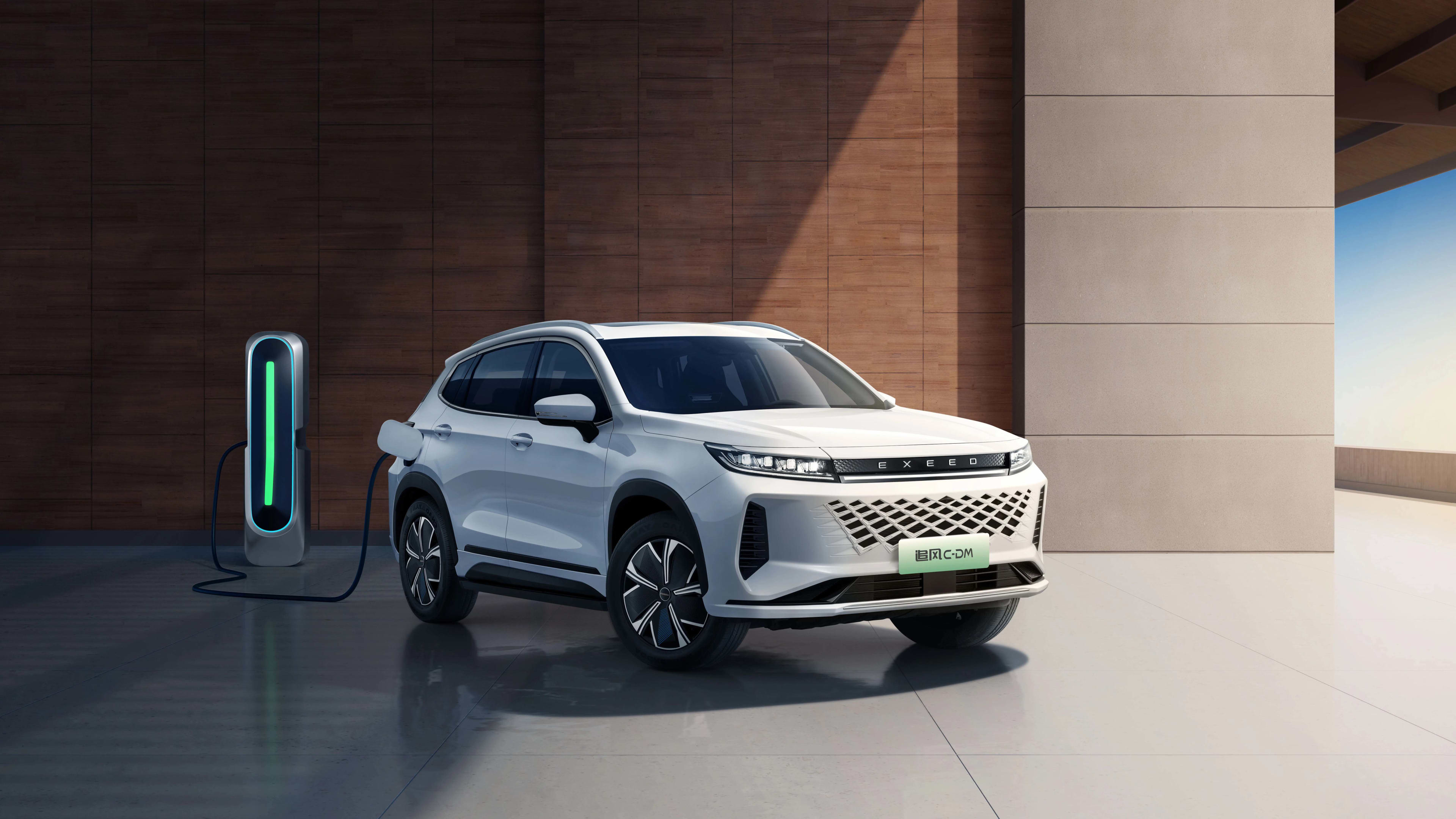 A white SUV plugged into an EV charger in front of a brick and concrete wall.