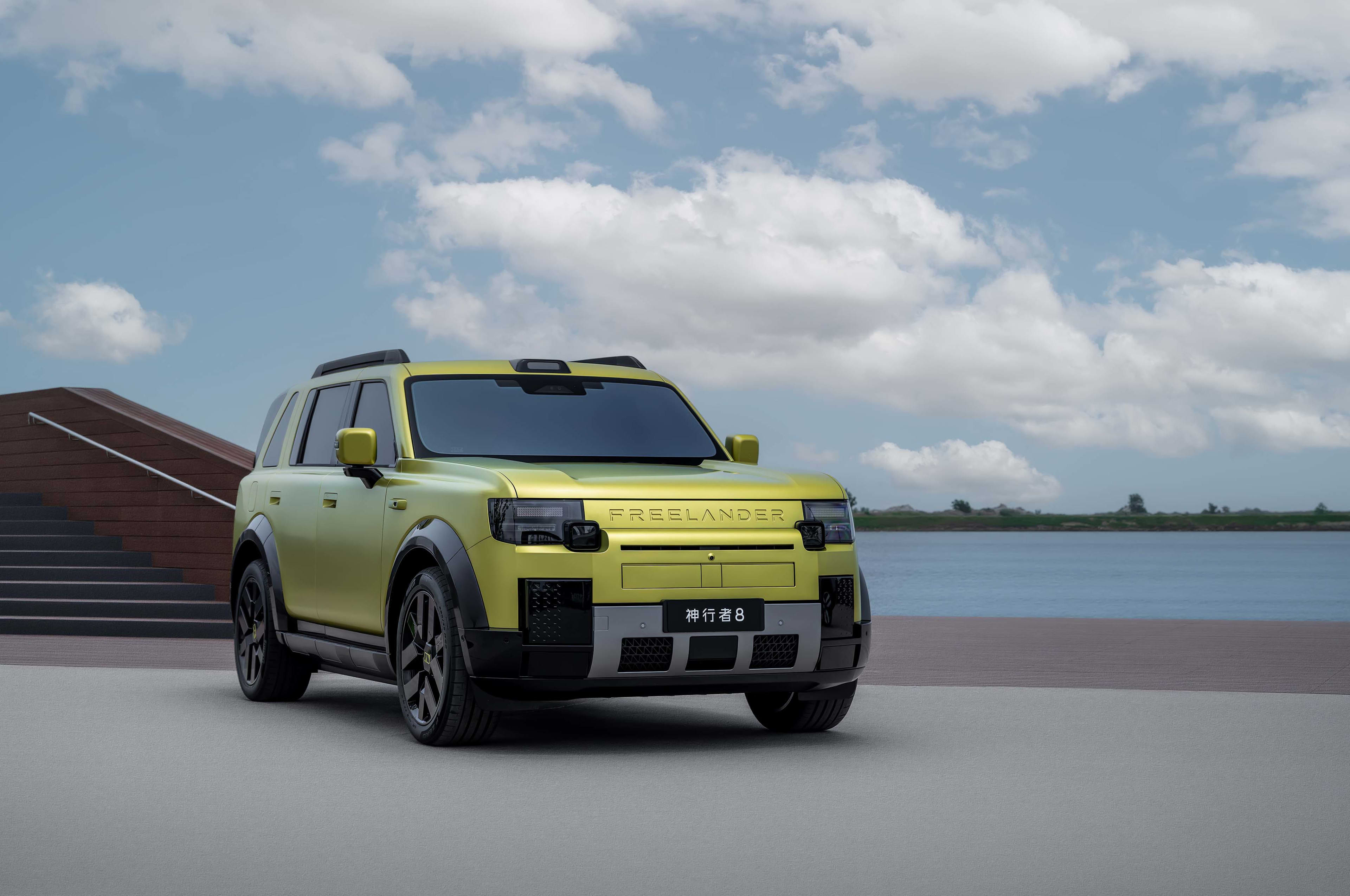 A yellow SUV parked on a concrete surface, with water in the background and clouds in the sky.