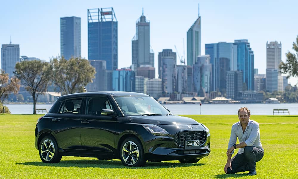 Alex Forrest posing with a black 2024 Suzuki Swift on the South Perth Foreshore