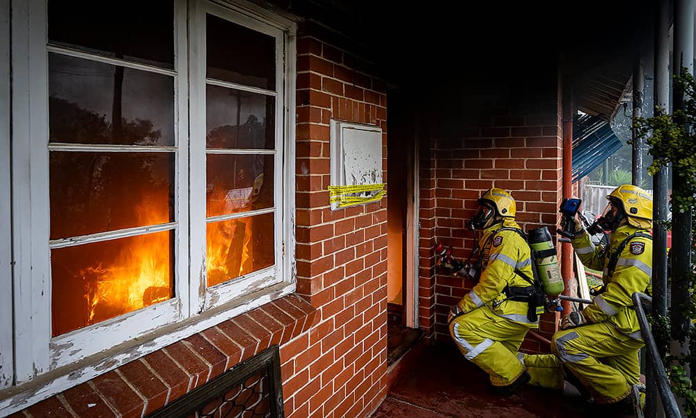 Two fire fighters spraying water into a home from the front door