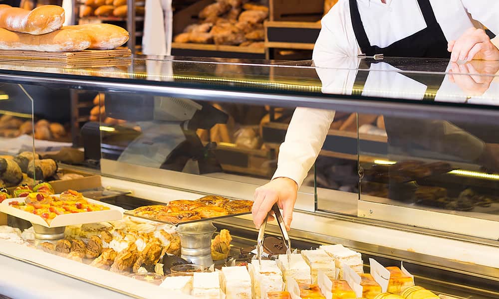 A bakery display cabinet with someone reaching in with tongs to get a cake