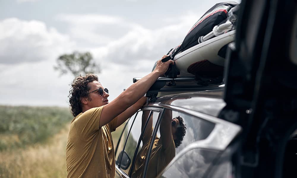 A man is checking the strapping on his loaded roof rack