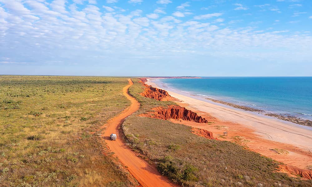 A car on a red dirt track near the ocean near Broome