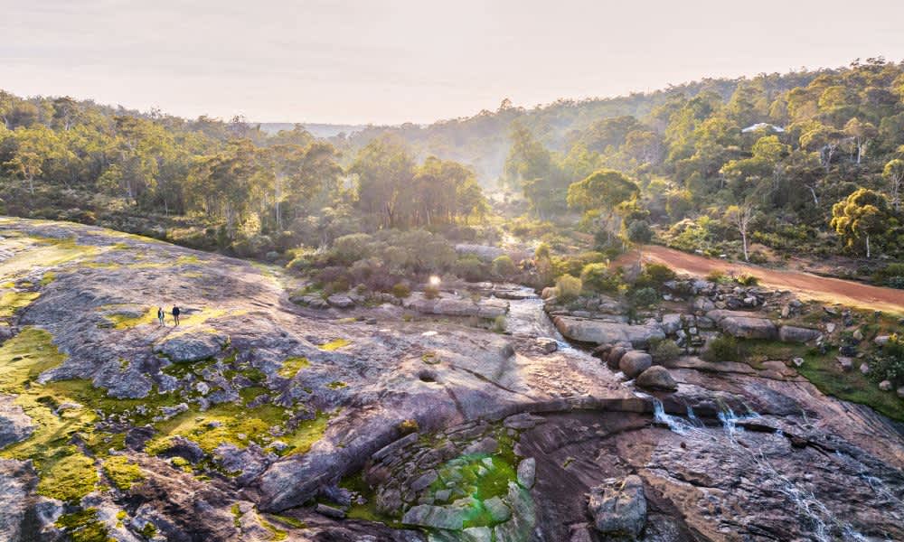 two people hiking in hills next to flowing waterfall