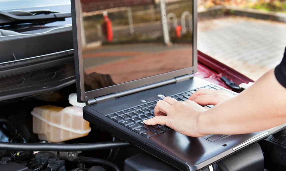 A man typing on a computer over an engine