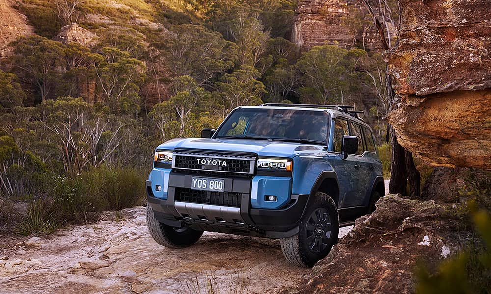 A blue Toyota Prado driving through a rocky landscape