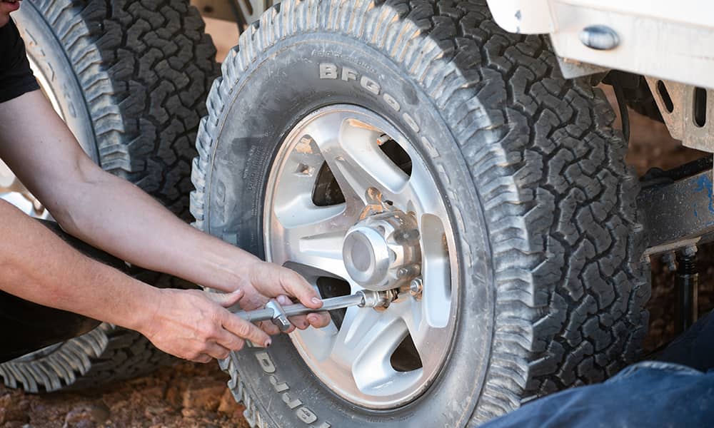 A pair of hands using a tool to loosen the wheel nuts on a caravan wheel in order to change a flat tyre