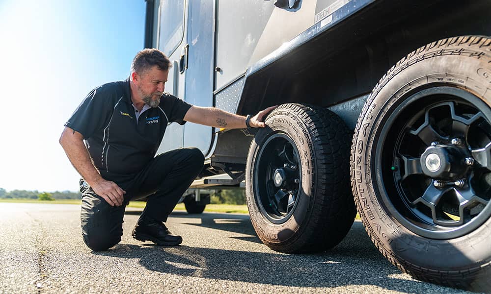 Man kneeling down beside caravan looking at the tyre