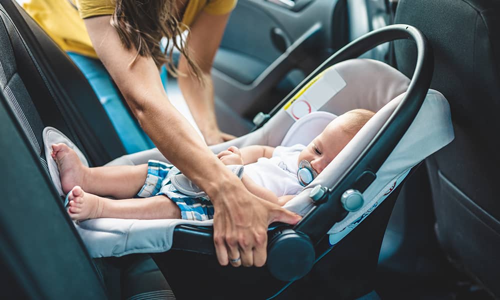 A rear facing child seat being handled by a parent in a car