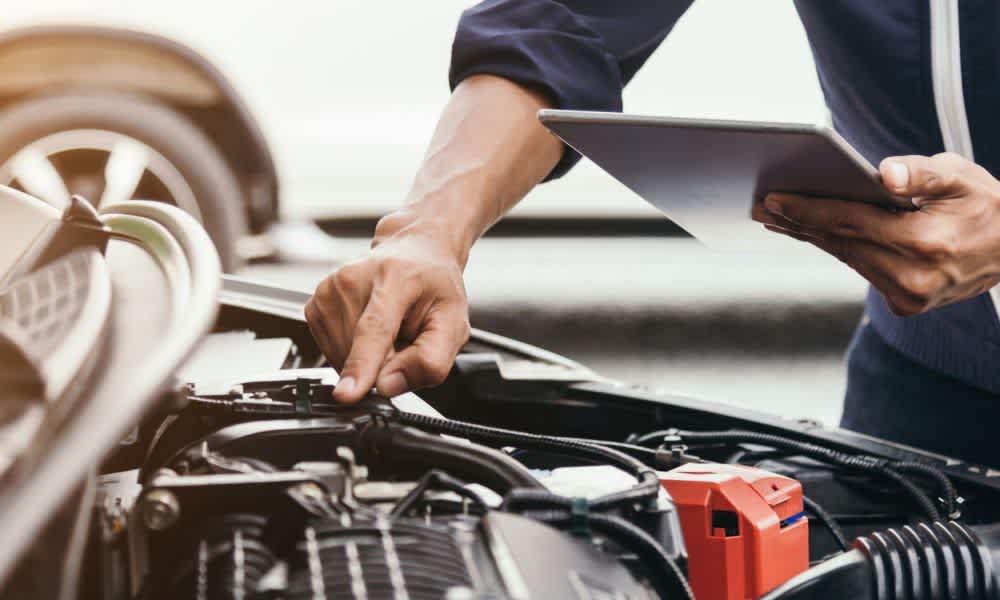 Man with hood of car open holding tablet inspecting car