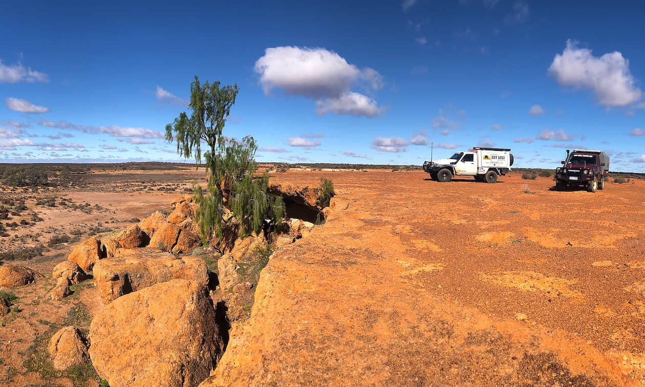 Two four-wheel drives on a high rock plateau overlooking a rocky dry landscape