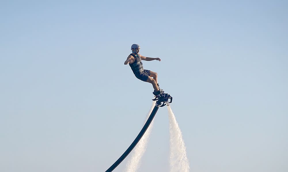 A man is airborne riding a flyboard device with waterjets shooting downwards