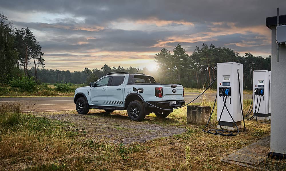 A white Ford Ranger EV parked at a charger in a country landscape