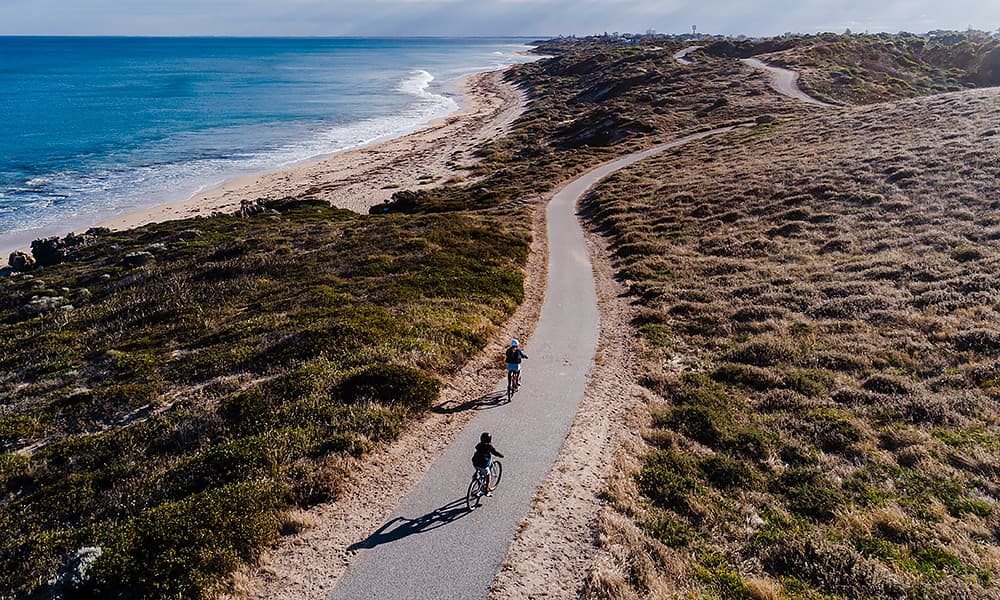 An aerial view of two children on a coastal bike path