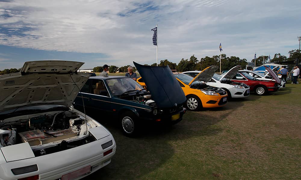A row of older cars with bonnets up showing EV motors and battery packs