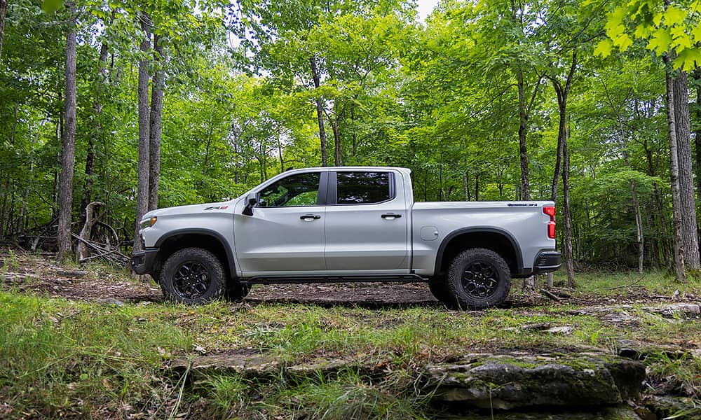 A white Chevrolet Silverado parked in a forest seen from the side