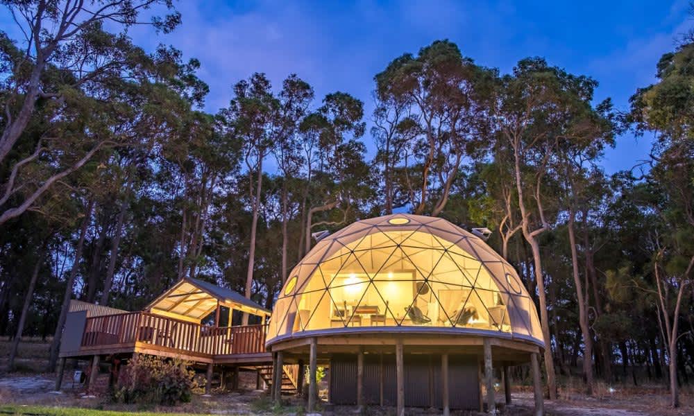 Dome-shaped glamping tent lit up in the evening among the forest