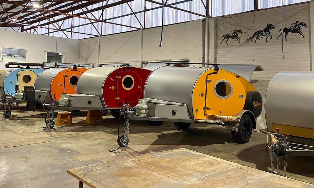 A row of teardrop campers in various colours in a factory setting