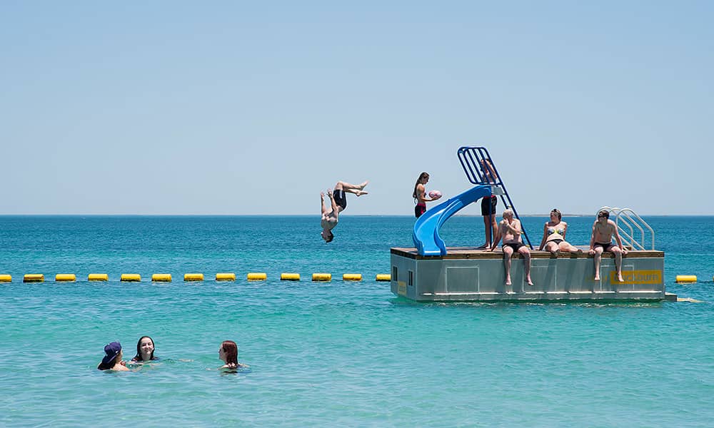 Kids swimming at the beach and one jumping from a pontoon