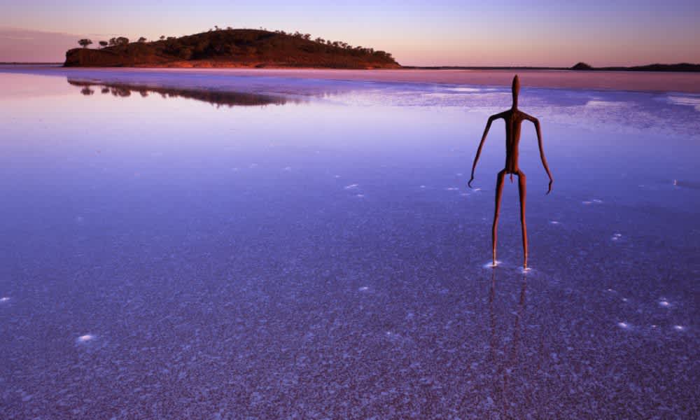 sculpture of a man standing in lake looking at island at sunset