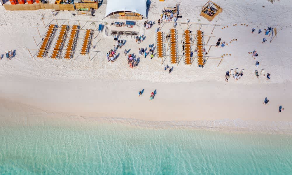 Tables and chairs set up for a lunch on the sand in front of turquoise waters in Geraldton