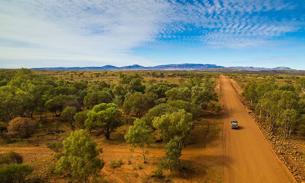 An aerial image of a car travelling down red dirt road